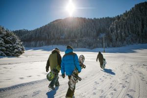 three people walking a snowing mountain to snowboard